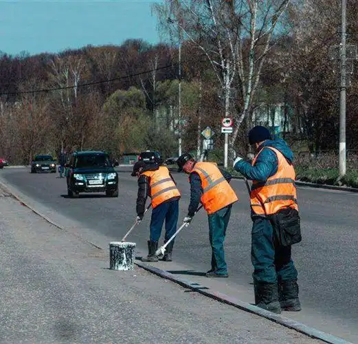 Road workers in high-visibility vests painting a roadside kerb