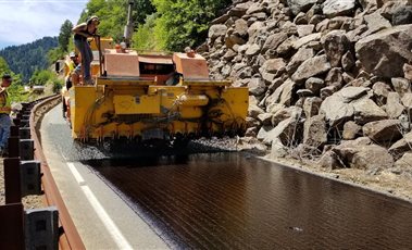 Geotextiles & Road Construction Materials Road construction machine laying a new road surface beside a rocky hillside
