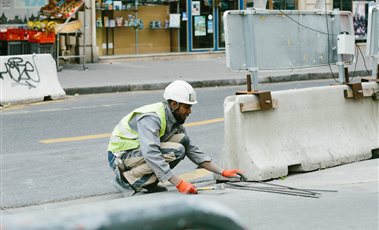 Worker in a hard hat and safety vest fitting a roadside concrete safety barrier