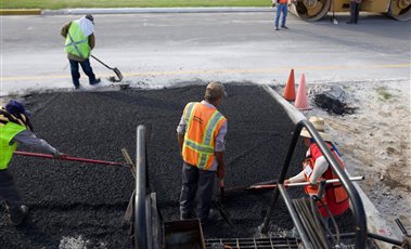 Road crew in high-visibility vests patching a road with fresh asphalt