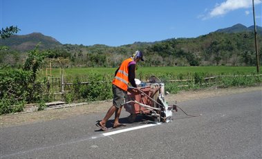 Worker in an orange safety vest applying a white road line with a road marking machine
