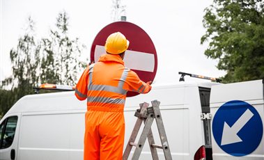 Technician in orange workwear installing a road sign from a ladder